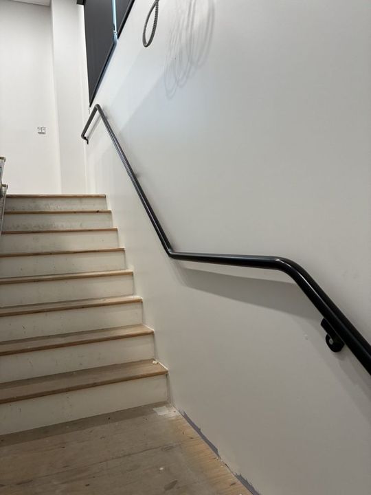 Black wall-mounted pipe handrail running up a stairwell in Blawnox